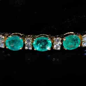 Luxury 18K yellow gold tennis bracelet featuring natural oval-cut emeralds totaling 9.27 carats accented with brilliant-cut diamonds.