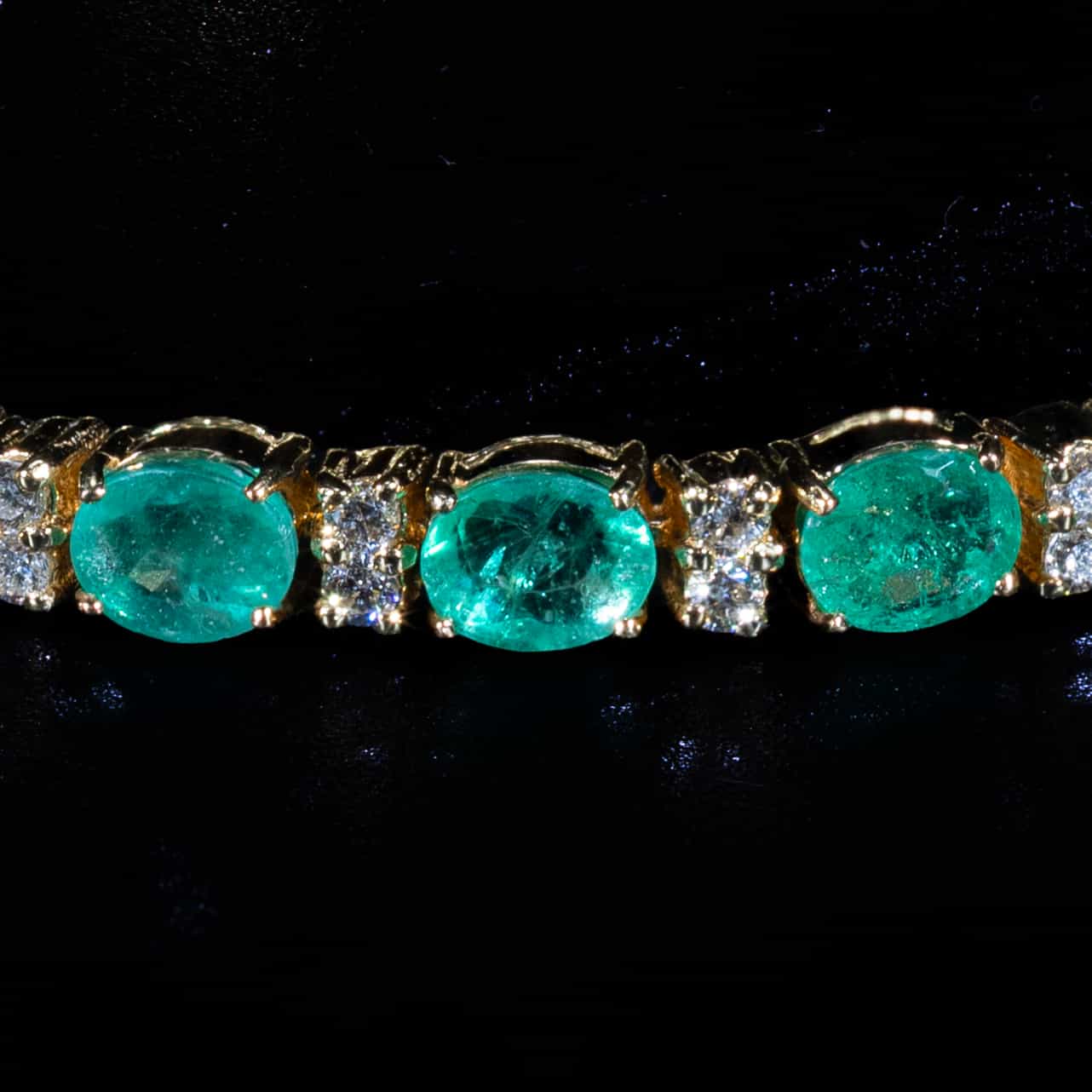 Luxury 18K yellow gold tennis bracelet featuring natural oval-cut emeralds totaling 9.27 carats accented with brilliant-cut diamonds.