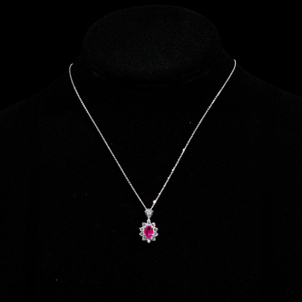 18K white gold pendant necklace featuring a natural oval ruby surrounded by a halo of brilliant-cut diamonds with a matching white gold chain.