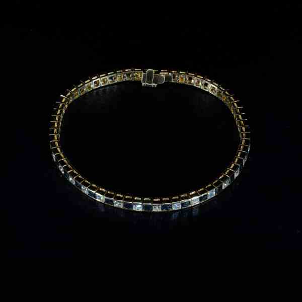 Luxury 18K yellow gold tennis bracelet featuring alternating natural princess-cut blue sapphires and brilliant-cut diamonds.