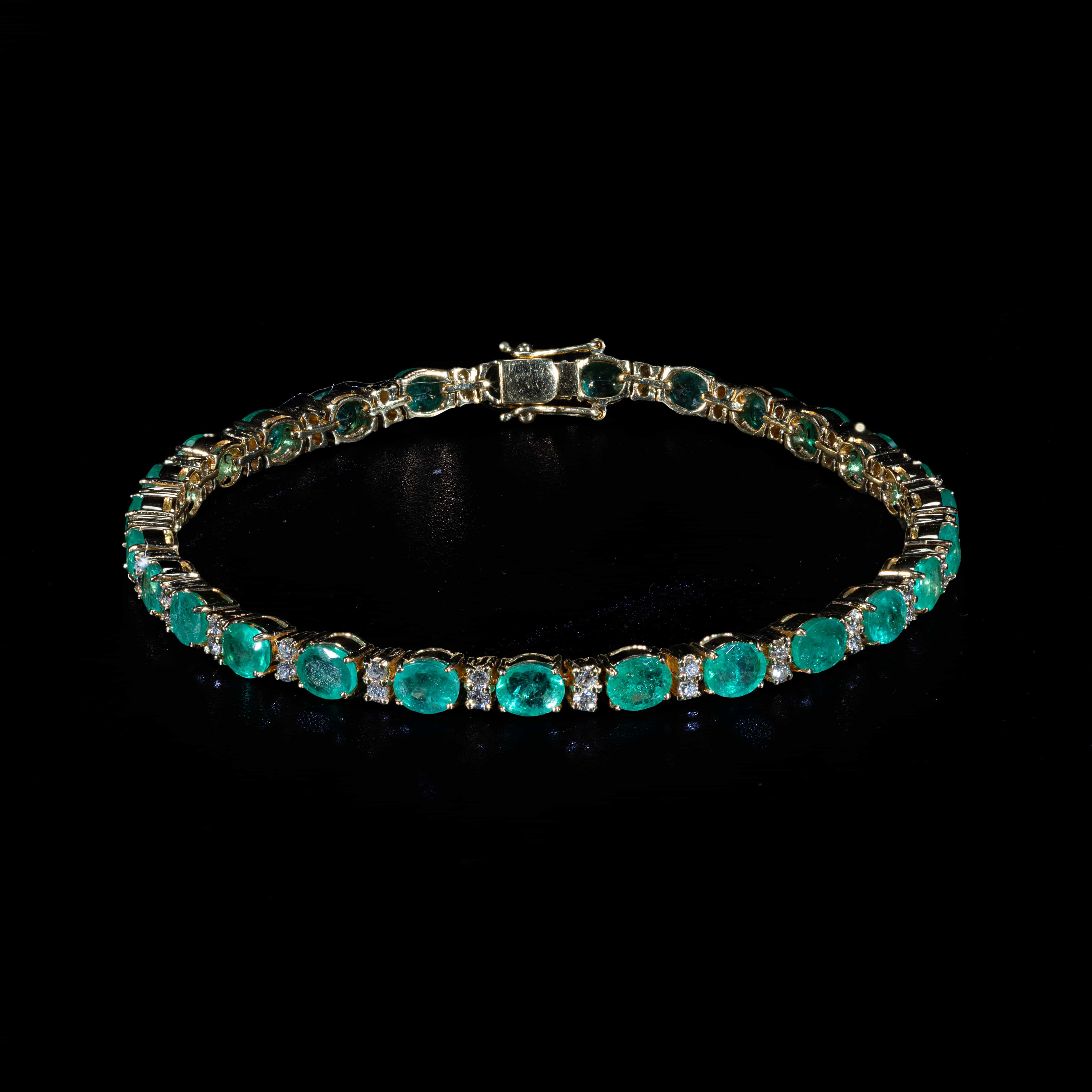 Luxury 18K yellow gold tennis bracelet featuring natural oval-cut emeralds totaling 9.27 carats accented with brilliant-cut diamonds totaling 1.00 carat.