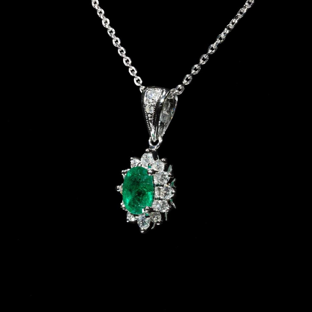 18K white gold pendant necklace featuring a natural Colombian emerald surrounded by a halo of brilliant natural diamonds suspended from a matching white gold chain.