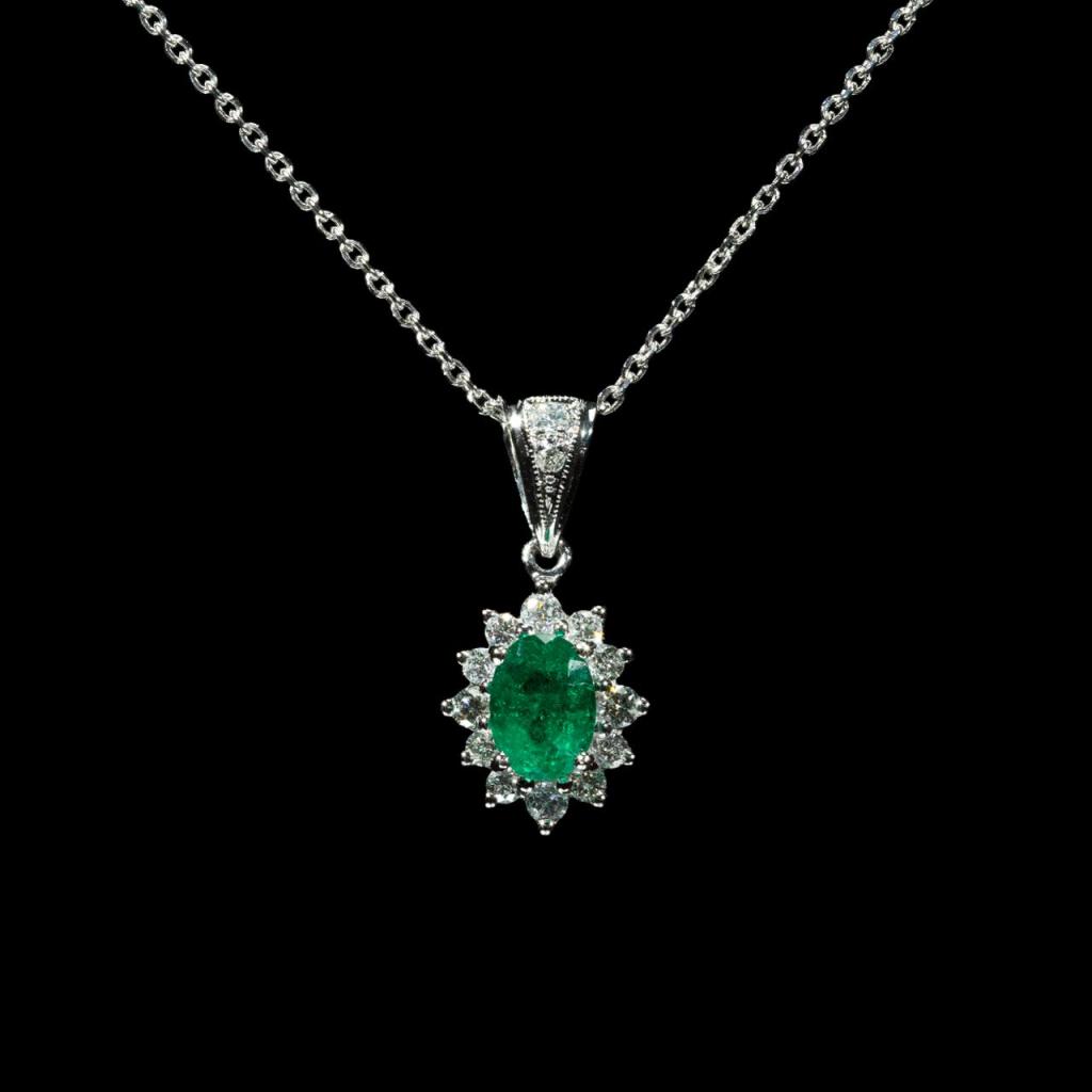 Elegant 18K white gold pendant necklace featuring a natural Colombian emerald surrounded by a halo of brilliant natural diamonds.